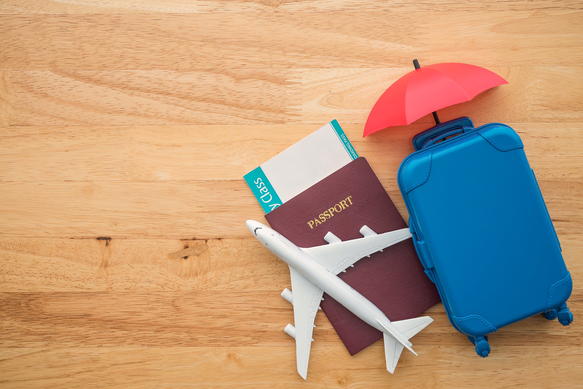 A passport, boarding pass and suitcase sheltered under a small umbrella