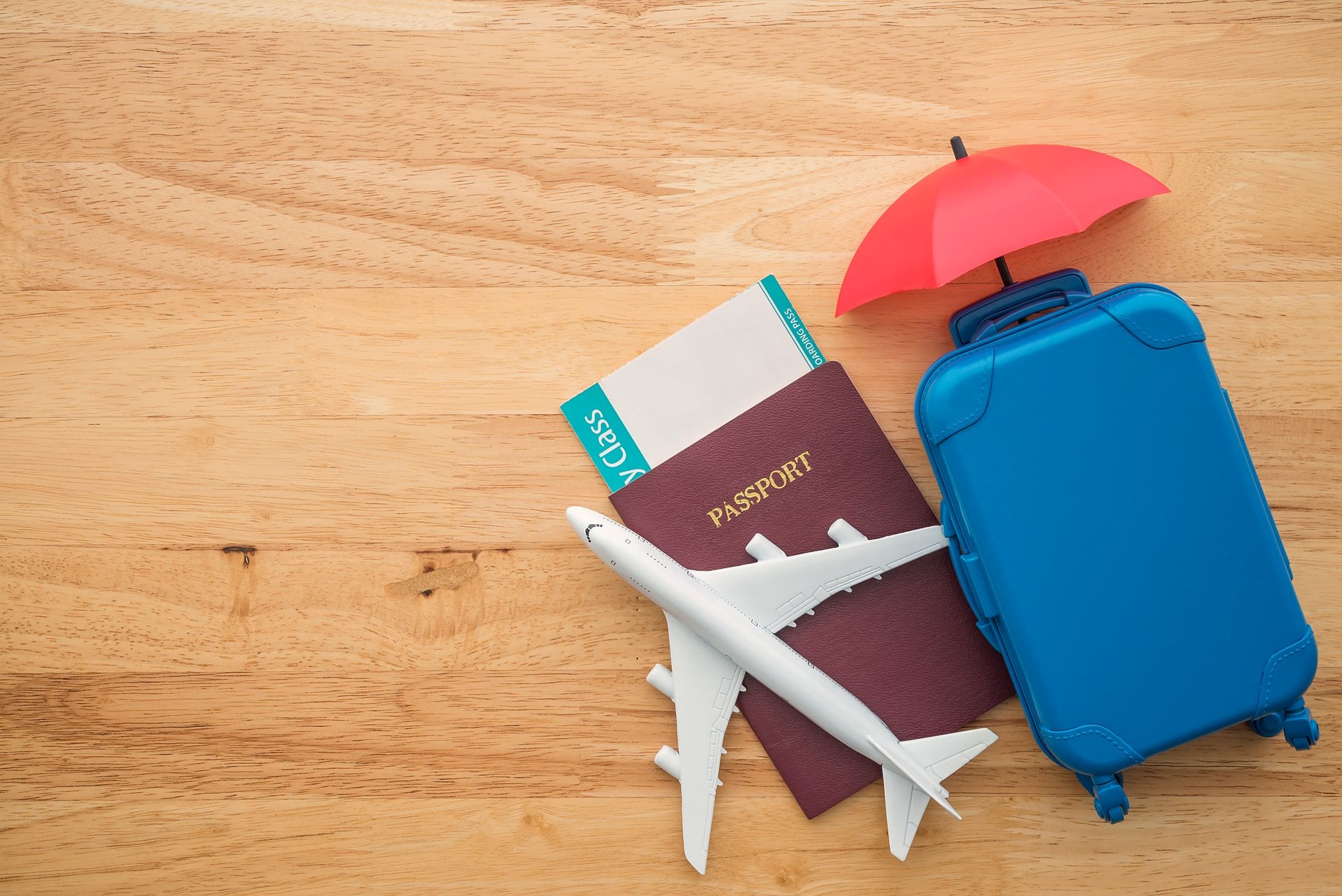 A passport, boarding pass and suitcase sheltered under a small umbrella