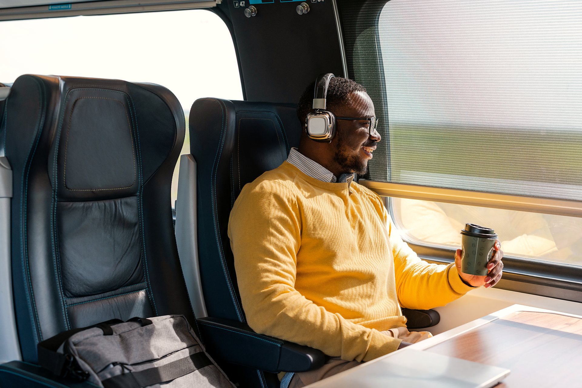 A young man travelling by train with headphones and a coffee
